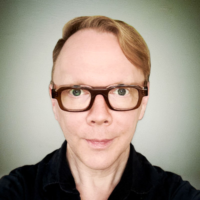 Portrait of myself; a white guy in his 40s with reddish-blond hair and thick-framed glasses, wearing a black shirt