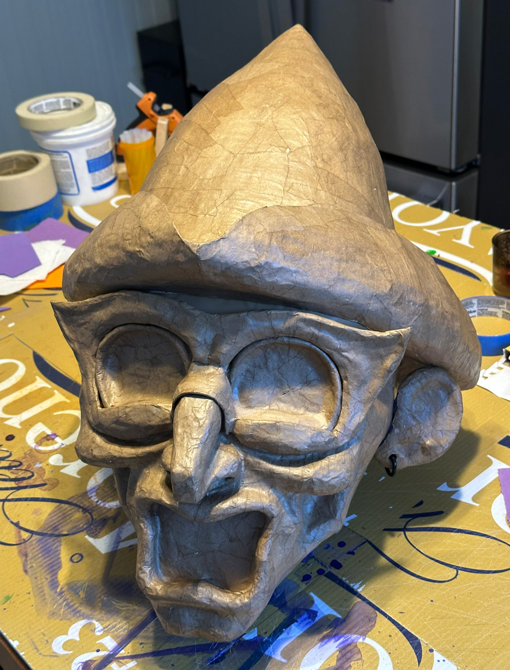 The head in brown paper mache wearing a brown paper mache hat