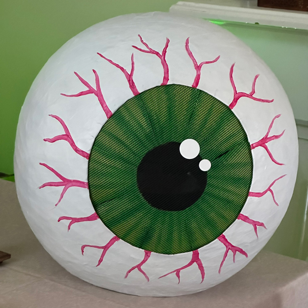 Close up of the finished eyeball mask; a big white orb with a green iris and black pupil, and pink veins going outward from the iris.