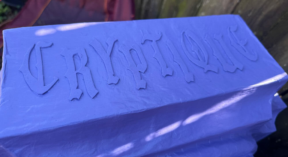 Close up of raised letters spelling Cryptique, spray painted purple.