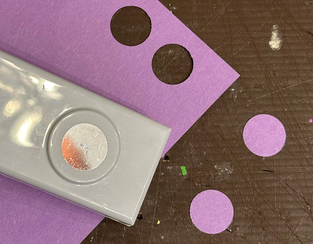 A large hole punch next to a piece of purple paper with  two circles cut out