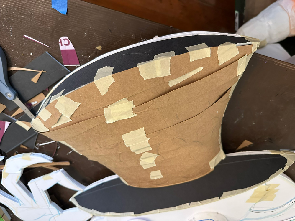 The hat now has strips of brown paste board taped across it, creating a 3D shape.