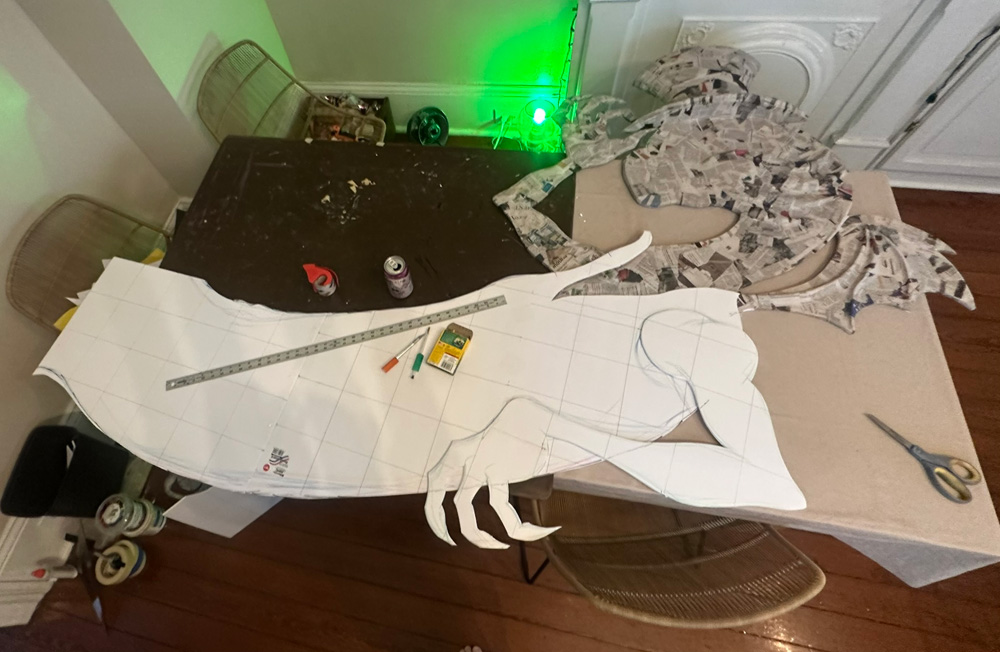 The head/neck/arm component of the Jabberwocky covered in newspaper, and laid in place onto the second component, which is the long torso piece, currently just a flat piece of foam board, with a flat foam board arm laying in place on that.