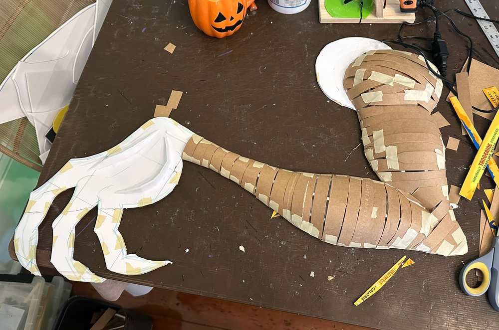The arm now has strips of brown pasteboard taped in place, defining the 3D shapes of the arm.