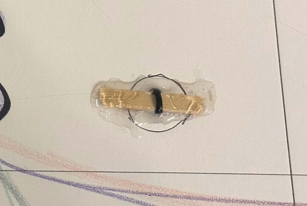 Close up of a small length of a wooden stick with a twist tie wrapped around it; it's inserted through a panel of foam board and covered with lots of hot glue.
