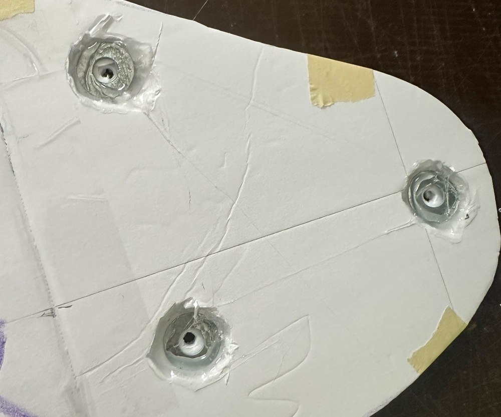 Three areas on the back of the foam board with metal washers hot-glued around holes.