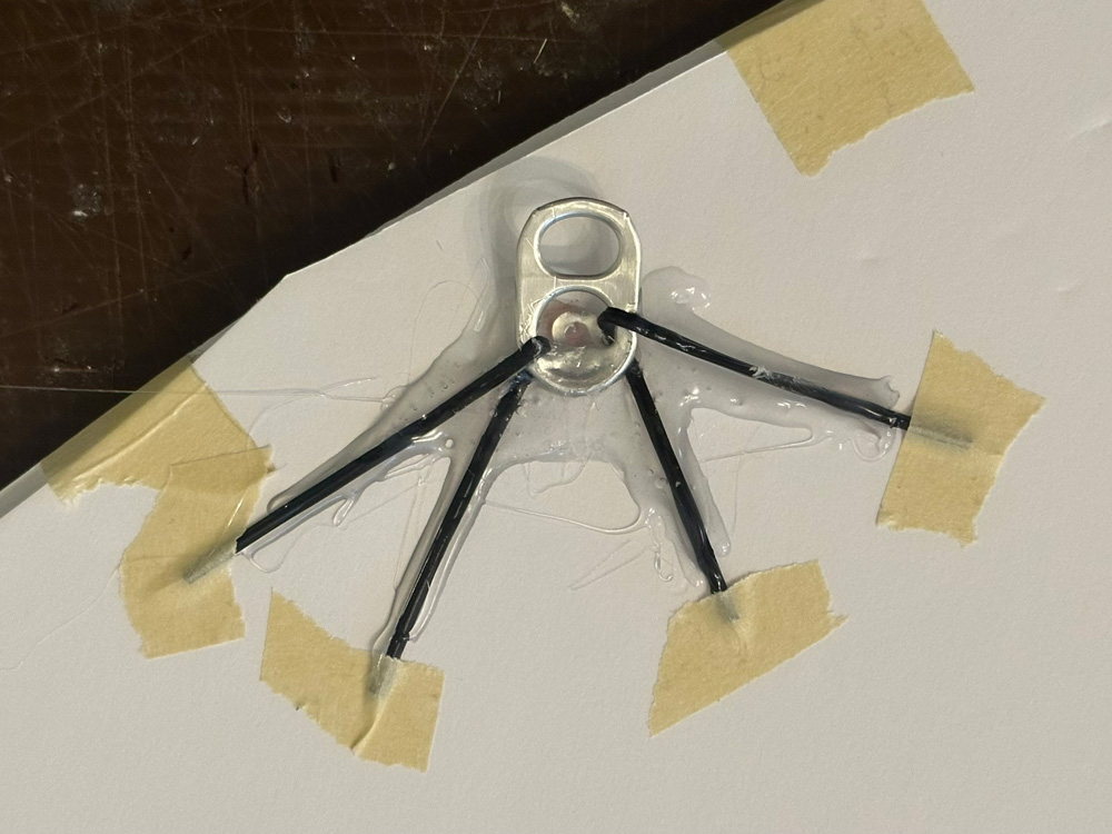 A soda can pull tab secured onto a piece of foam board with twist ties and lots of hot glue.