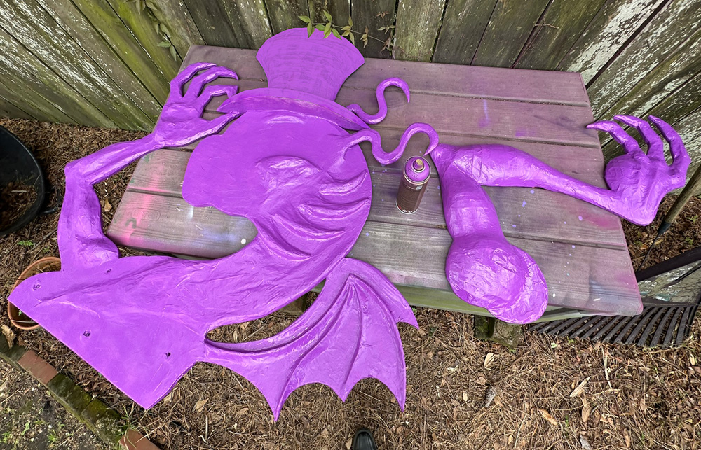 The head/neck/arm/wings component of the Jabberwocky, and the arm, laying on a big plastic box and spray painted a bright pink/purple color.