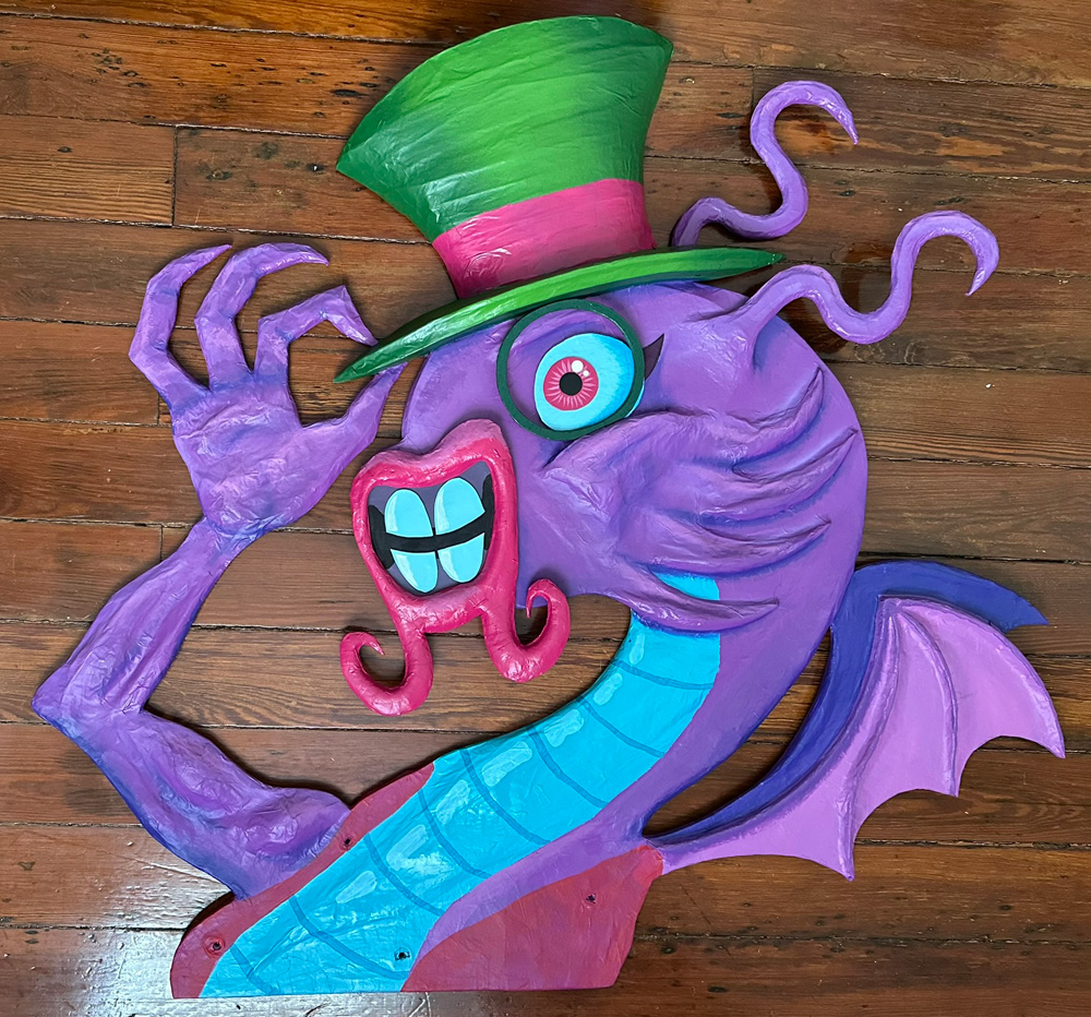 The head/neck/arm/wings component with painting completed; it's mostly purple, with a green top hat with a pink band, pink lips, light blue teeth, a dark green monocle, and a teal area along the front of the neck and chest.