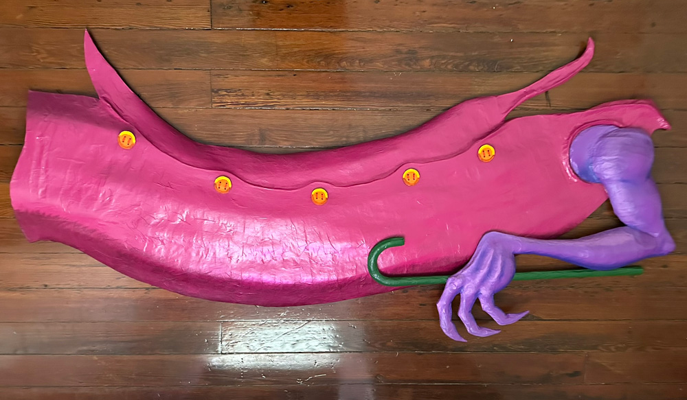 The Jabberwocky's torso with painting completed; it's a bright red/pink color with orange buttons; one purple arm is attached holding a green cane.