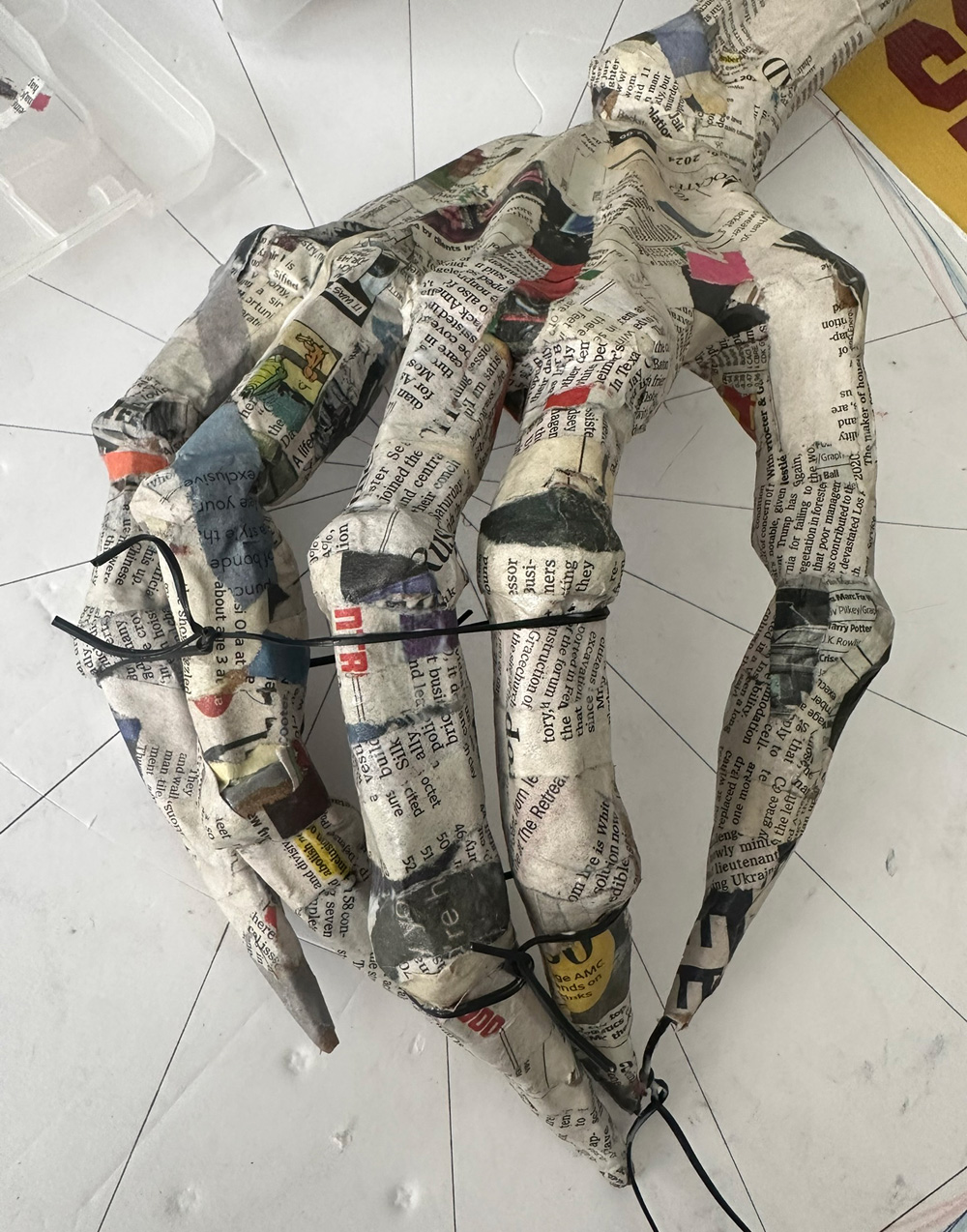 Close up of the hand covered in newspaper and with twist ties wrapped around the fingers to hold them in position.