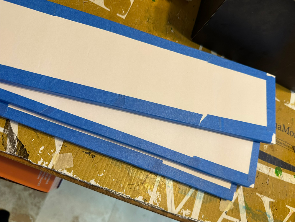 Rectangular slats of foam board with blue painter's tape on the edges.