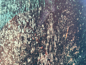 Close up of a scratched metal texture on a light pole which has been painted various colors and all of the paint is very weathered; it's mostly very dark greenish black with some visible spots of lighter green and brown